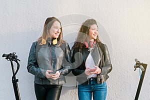 Two multiethnic female friends on electric scooters using smartphone outdoors