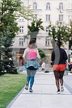 Two multiethnic girls running through the city streets, outdoor communicating.