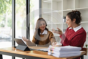 Two multiethnic professionals colleagues working together with laptop and papers in office. Female mentor and young