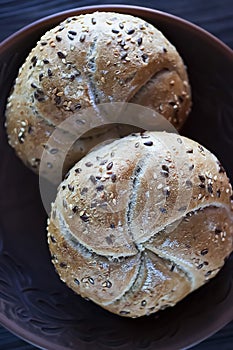 Two multigrain buns with sesame seeds and flaxseed on a brown plate.