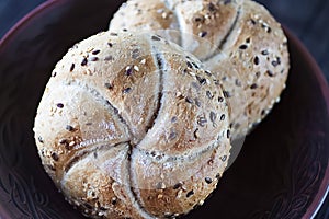 Two multigrain buns with sesame seeds and flaxseed on a brown plate.