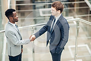 Two multiracial businessmen handshaking in modern office for end of great deal