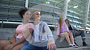 Two multiracial couple of teenagers sitting stairs outdoors, romantic youth