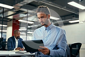 Two multiracial men in businesswear using digital tablet during meeting in office