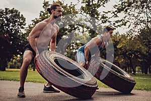 Two muscular men flipping tires in the park