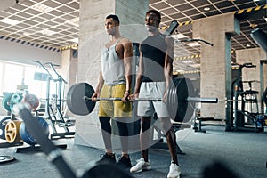 Two muscular men poses with heavy barbell in gym