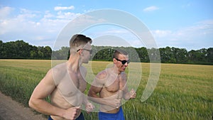Two muscular men running and talking outdoors. Young smiling athletic guys jogging over the field. Male sportsmans