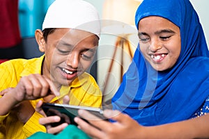 Two muslim sibling kids busy using mobile at home - concept of kids using technology, internet and social media