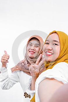 Two muslim woman wear hijabi taking selfie from smartphone isolated over white background