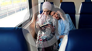Two Muslim women traveling by train, one woman reads, another talking on the phone