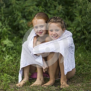 Two naughty little girls sitting on the beach in a towel after a bathe in the lake. Summer.