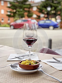 Two near glasses of red wine, bottle of wine and chef`s compliment, small plate of paella served on table outdoor