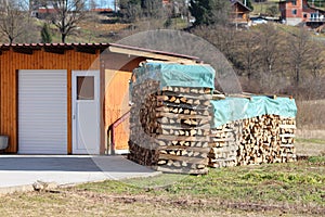 Two neatly stacked piles of firewood covered with thick nylon protection left to dry in family house backyard