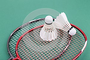 Two new badminton shuttlecock with rackets on green mat court