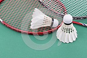 Two new badminton shuttlecock with rackets on green mat court