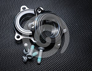 Two new hub bearings with spare mounting bolts, for a sports car. Black background, metal mesh