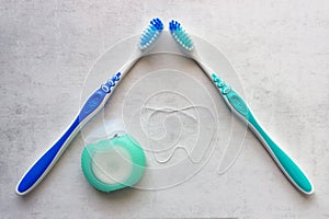 Two new toothbrushes  and container of dental floss. Dental floss laid out in the shape of a tooth. Tools for personal oral hygien