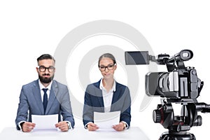 two newscasters with papers sitting in front of camera,