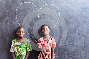 Two Nice Cute African Black Girls Standing in Front of Blackboard with Big Heart Love Symbol