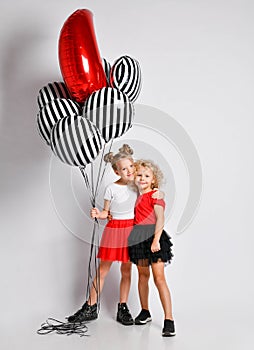 Two nice smiling kids girls in skirts and t-shirts with big air balloons stand together hugging