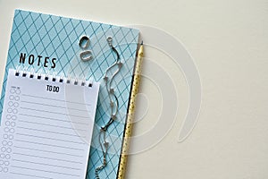 Two notepads with pencil, silver bracelet and earrings on a beige paper background. Top view. Close-up.