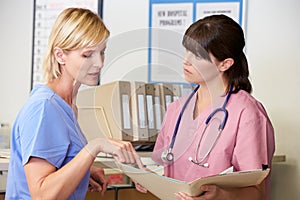 Two Nurses Discussing Patient Notes At Nurses Station