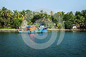 Two ocean fishing boats along the canal Kerala backwaters shore with palm trees between Alappuzha and Kollam, India