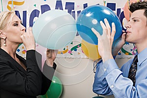 Two office workers blowing up balloons