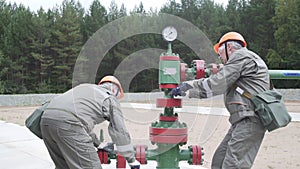 Two oil field technical workers closing valve of x-mass wellhead to shut off well. Decline in oil production after