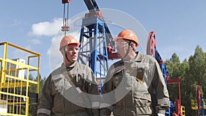 Two oil workers overseeing drilling rig of crude oil production. Industrial oil well pump jacks pumping crude oil for