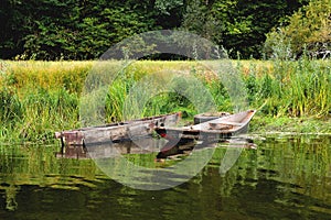 Two old boats on the shore are tied to an old car wheel, on a background of green grass