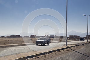 Two old cars are driving along the road along the desert and a s
