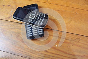 Two old cellphones stacked against a wooden background,