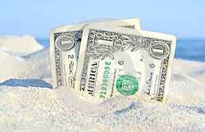 Two old dollar bills in sand on background of sea blue sky on sunny summer