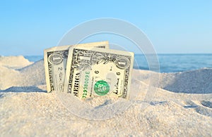 Two old dollar bills in sand on background of sea blue sky on sunny summer