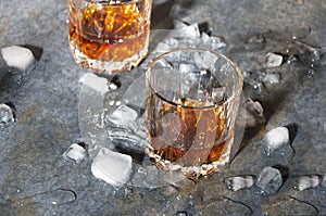 Two old fashioned glasses with whisky and ice cubes on bar counter. Hard light and shadows