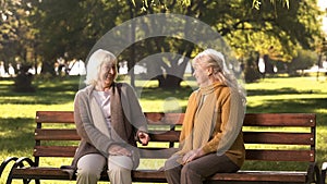 Two old fiends talking and laughing sitting on bench in park, retirement age