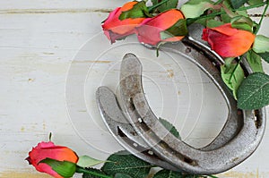 Two old horse shoes paired with silk red roses on a white-washed rustic wooden background photo