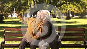 Two old ladies taking selfie on mobile phone sitting on bench in park technology