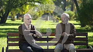 Two old men with walking sticks sitting on bench in park and thinking about life