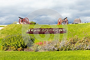 Two old red and black cannons looking over hill with the Quebec motto Je me souviens (I Remember) in floral bed