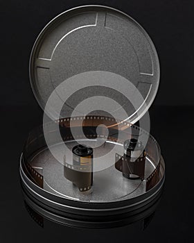 Two old rolls of analog photographic film in a circular tin container with the cap open and some negatives inside