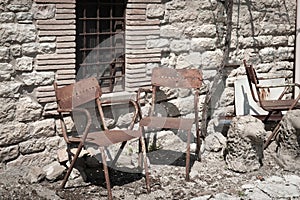 Two old rusty chairs outside stone wall on street