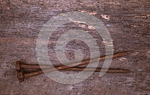 Two old rusty nails rest on a wooden background. Construction concept or religious theme