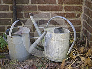 Two old rusty tin watering can in cemetery wall