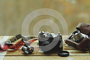 Two old school vintage photo cameras and scattered films on light brown table. One in brown retro leather case holder. Blurred