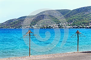 Two old straw umbrellas on the beach. Nice view of Salamis island in Greece.