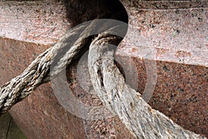 Two old textured ropes stick out of a hole in brown marble stone monument