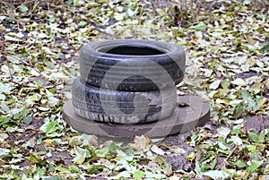 Two old used car tires are lying on the concrete manhole cover