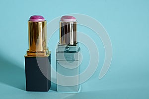 Two old used tubes of lipstick stand on a blue background.